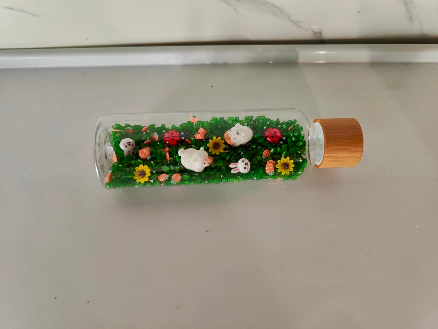 Bouteille sensorielle inspirée de la nature avec fleurs, insectes, moutons, vaches. Effet visuel doux, sonore et relaxant. Créée à la main en France.