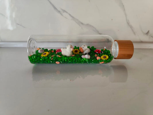 Bouteille sensorielle inspirée de la nature avec fleurs, insectes, moutons, vaches. Effet visuel doux, sonore et relaxant. Créée à la main en France.