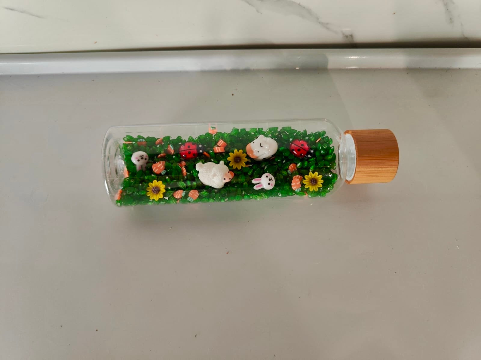 Bouteille sensorielle inspirée de la nature avec fleurs, insectes, moutons, vaches. Effet visuel doux, sonore et relaxant. Créée à la main en France.